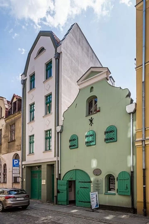 Zielony smukły budynek, czyli Muzeum Podr&oacute;żnik&oacute;w w Toruniu, kt&oacute;ry mieści się w zabytkowej kamienicy.